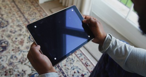 Mid section of african american man holding a digital tablet with copy space at home. staying at home in self isolation