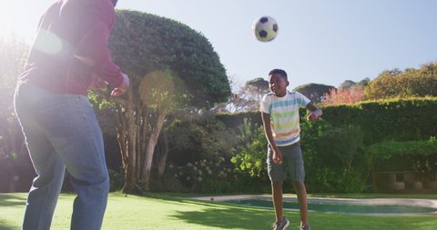 African american dad and son playing with football together in the garden on a bright sunny day. fatherhood and love concept