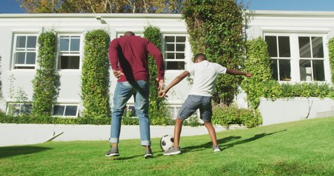 African american dad and son playing football together in the garden on a bright sunny day. fatherhood and love concept