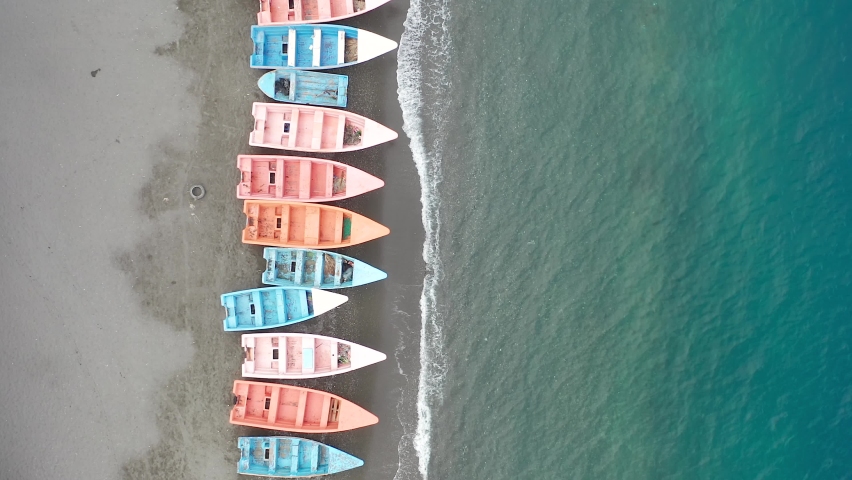 Aerial drone forward view along Palmar de Ocoa beach with colorful pink and blue small boats on sea shore. Dominican Republic