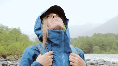 Portrait of young female hiking on a rainy day. Woman on a hike by the river under heavy rain 