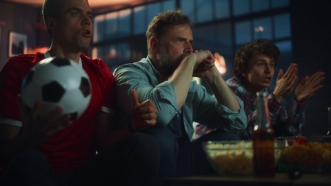 Night At Home: Three Joyful Soccer Fans on a Couch Watch Game on TV, Celebrate Victory when Sports Team Wins Championship. Friends Cheer for Favourite Football Club Play. Low Angle Slow Motion