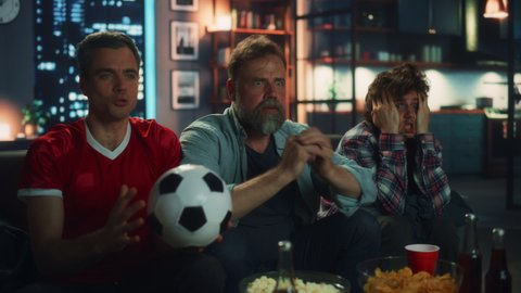 Night At Home: Three Joyful Soccer Fans Sitting on a Couch Watch Game on TV, Celebrate Victory when Sports Team Wins Championship. Group of Friends Cheer for Favourite Football Club Play. Slow Motion