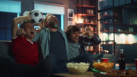 Night At Home: Three Joyful Soccer Fans Sitting on a Couch Watch Game on TV, Celebrate Victory when Sports Team Wins Championship. Group of Friends Cheer When Favourite Football Club Play.