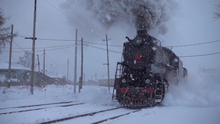 Gimbal heavy snow blizzard old train steam locomotive rides in slow motion by rail railway railroad. Epic impressive steam engine wheel mechanism. Siberia Russia travel transsib. Beautiful snowfall