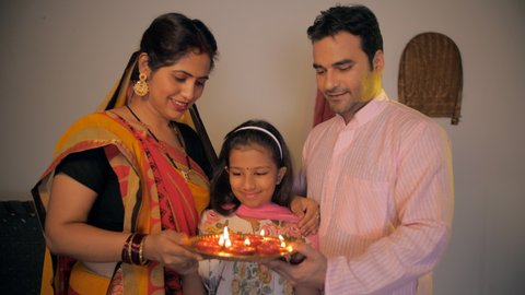 Village scene of an Indian family happily doing aarti arti - Puja at home. Medium shot of an attractive village couple celebrating the festival of Diwali together with their cute daughter