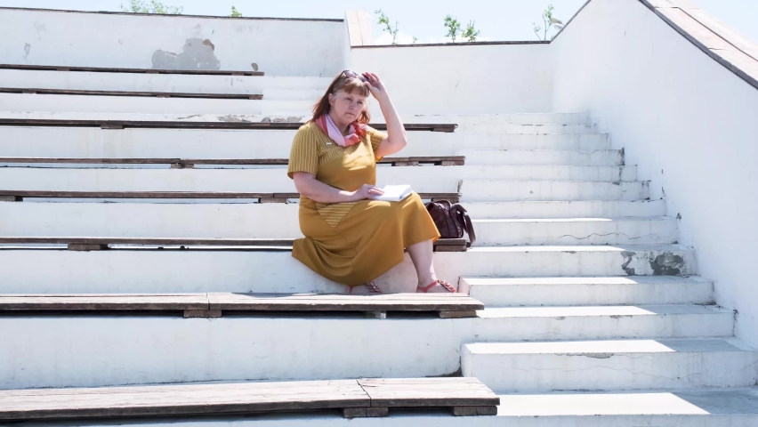 elderly woman sits on the bench of an abandoned open-air cinema