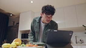 Young mixed race male cooking dinner at home searching recipe on laptop 