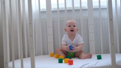 A small child plays in his crib with colored cubes and builds a pyramid out of them.