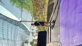 Vertical video. Slowmotion shot. A young woman is having fun in a trampoline park in tropics. Shot on a phone