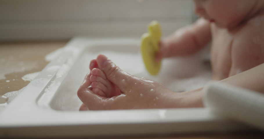 Mother and daughter spend time at home together. Young mom helps her adorable little child to take a bath in a kitchen sink. Adorable girl have fun in the water and foam. Royalty-Free Stock Footage #1074442055