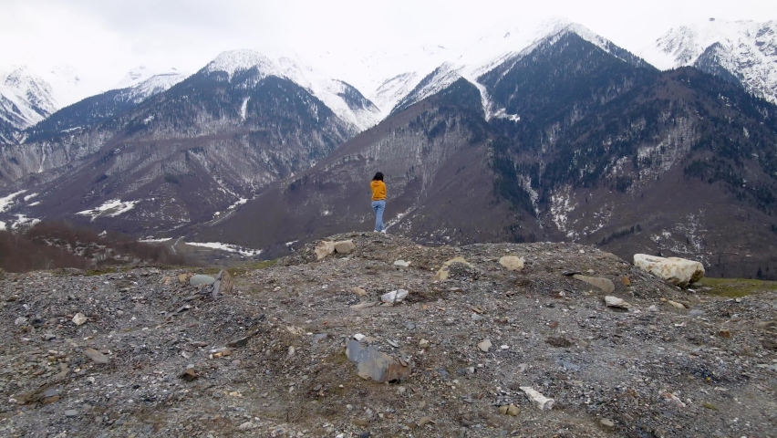 Drone footage. A young girl is enjoying an incredible mountain panoramic landscape. Snowy peaks of the mountains. An exciting journey.