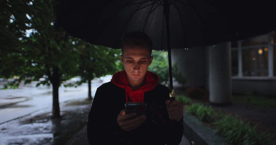 Man walking at alley under umbrella using smartphone, slow motion