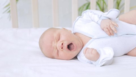cute yawning little newborn baby boy in the nursery on the white cotton bed at home, healthy baby sleep concept