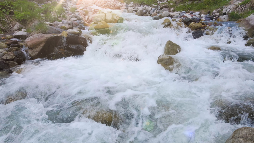 Rapid creek stream and rocks river flowing through the meadow and cascade of the stones. Clean cold water hits the stones and flights with the many splashes. Sunlight shines at the sunset. Royalty-Free Stock Footage #1074468044