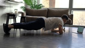 Determined fitness blogger doing ABS exercises in home interior shooting vlog tutorial via blank netbook technology with copy space area for your website, man watching sportive video on laptop