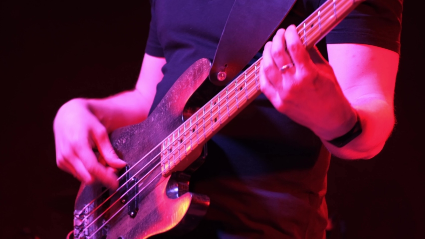 Male guitarist playing electric bass guitar on a rock concert in a club. Red lighting, hands closeup. Royalty-Free Stock Footage #1074469823
