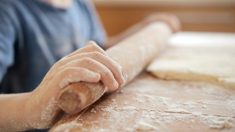 Closeup of little child using wooden rolling pin for preparing pizza dough