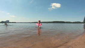 A beautiful little girl goes ashore with a swimming circle. Beach and sun. Summer day. Holiday. Learn to swim. Hot weather. Video.