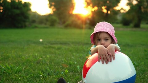 summer, vacation, nature, happy childhood - one small toddler preschool child smiling kid girl in pink hat sit posing looking at camera play with big inflatable in park on meadow at sunset fresh air
