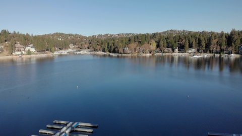 Aerial view flying out over Lake Arrowhead docks towards the forest and lakefront houses on a sunny winter day in Los Angeles, California, USA - Low Altitude shot
