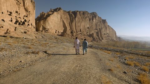 Bamyan , Afghanistan - 11 06 2020: Two Men Walking On Bamyan Valley With View Of Bamyan Buddha Site