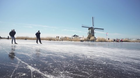 Leiden , Zuid Holland , Netherlands - 02 05 2021: Ice skating on frozen Dutch canals near traditional windmills, winter scenery