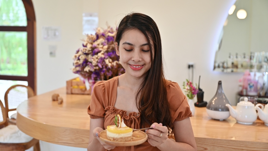 Attractive young asian woman happily eating lemon cheesecake at counter in cafe