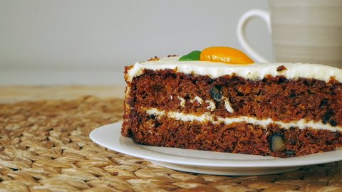 A slice of carrot cake with nuts and white cream on a plate on the kitchen table. Carrot homemade cake eaten with a fork