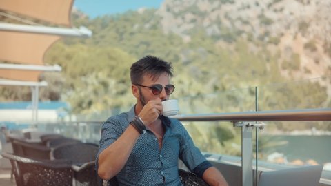 Attractive Businessman In Sunglasses. Businessman Drinking Tea On Vocation Resort. Man Sitting On Cafe Sea Beach. Guy Relaxing At Holiday Trip In Turkey Antalya. Handsome Italian Man Drinking Coffee