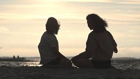 Slow motion 4K video of silhouette of mother and daughter sitting on beach during sunsetduring sunset at Baltic sea