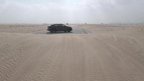Dubai , United Arab Emirates - 11 15 2020: Black Lamborghini Urus driving amid sand dunes on desert road in Dubai, aerial