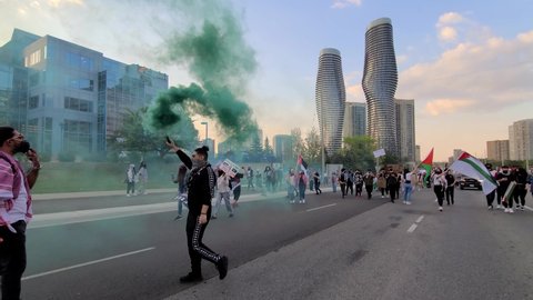 Mississauga , Canada - 05 18 2021: A demonstrator holding green smoke bomb for pro-Palestinian rally in Mississauga with the rest waved their Palestinian flags in the background to create awareness of