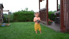 Portrait of adorable toddler little boy with a video camera in his hands. A child examines the camera while walking in the backyard in the village. Little photographer