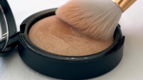Big lush brush gains powder, bronzer and highlighter on pile to be used in make-up. Artist working with face palette. Details of working process, tools in beauty industry. Decorative cosmetics.