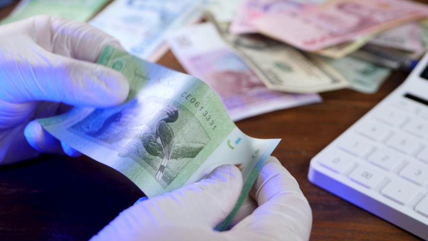 Cashier inspection or verification malaysian MYR ringgit for counterfeit money. Banknote bill currency of Malaysia. Money or cash revenue. Hand in white gloves under blacklight or ultraviolet | Shutterstock HD Video #1074528461