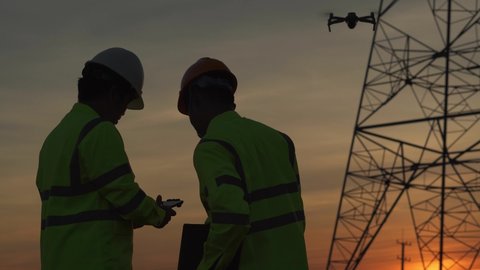 Silhouette of engineer Teams forcing a drone To inspect high voltage poles during the sunset time and Show success after work is completed.	