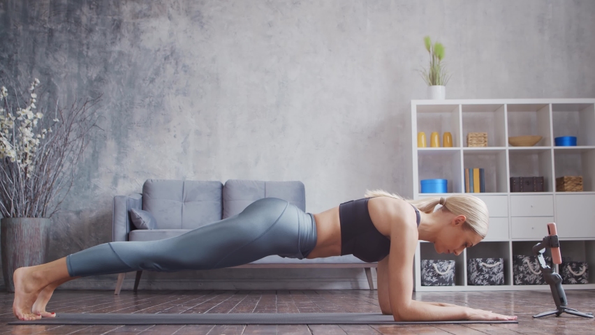 Young and sporty girl in sportswear is doing exercises in home interior. Fit and slender blond woman goes in for sports and fitness. Healthcare, fat burn and wellness.