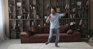 Happy lively single guy listens to music through headphones holding smartphone watch video clip, social media platform vlogger recording on mobile phone his dance for internet channel, fun concept