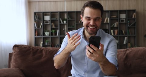 On-line bet, internet auction winner celebrate victory showing thumbs up. Millennial man sit on sofa holding smart phone check e-mail app read unbelievable news, got commercial offer feels overjoyed