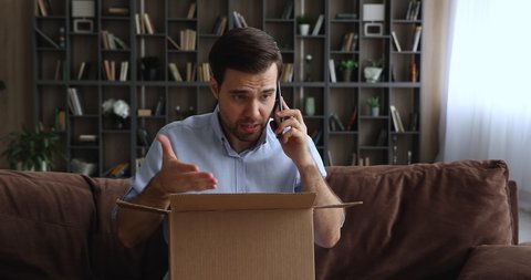 Man sitting on sofa with opened parcel express complaints to seller or courier on the phone about damaged goods, crashed items inside cardboard box. Dissatisfied e-commerce customer, claims concept