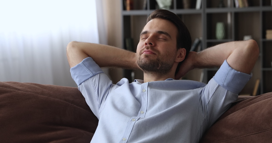 Close up serene calm millennial smiling man put hands behind head lean on comfy sofa resting alone at home, feel satisfaction enjoy fresh conditioned air inside of cozy living room, relaxation concept Royalty-Free Stock Footage #1074542453