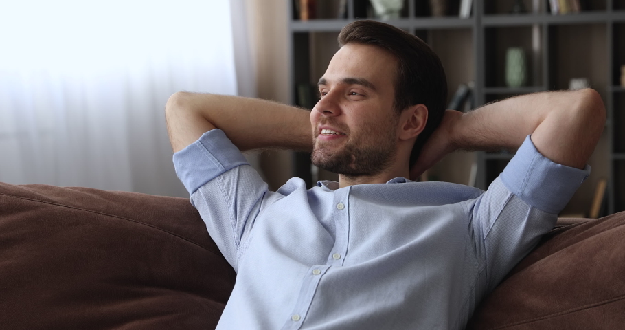 Close up serene calm millennial smiling man put hands behind head lean on comfy sofa resting alone at home, feel satisfaction enjoy fresh conditioned air inside of cozy living room, relaxation concept | Shutterstock HD Video #1074542453