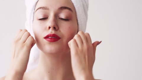 Facial exercise. Skin rejuvenation. Anti-aging massage. Facelift training. Woman in white towel stimulating building lift face muscles with fingers after shower isolated on light.