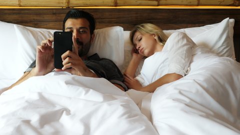 Man using phone texting message with girl during wife sleeping then wife wake up and want to see smart phone Husband hiding phone and don't give mobile phone to her. Wife upset, husband don't care