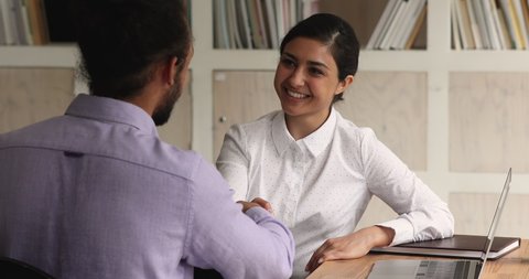 Smiling indian ethnicity businesswoman shaking hands with african american male partner, making agreement or thanking for help at office meeting. Happy female leader praising biracial employee.