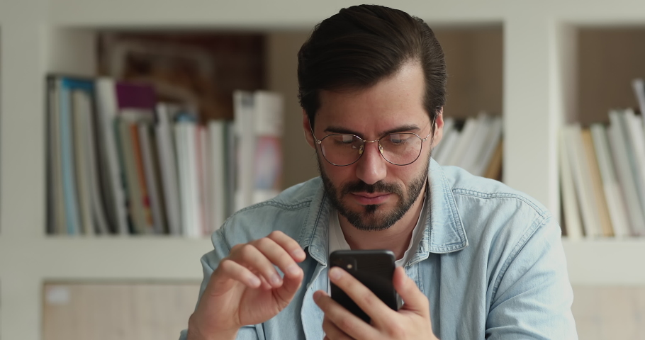 Anxious young caucasian man in glasses stressed of bad internet work, getting message with negative news or scam spam email, feeling unhappy with lost data or having problem with mobile gadget. Royalty-Free Stock Footage #1074550721
