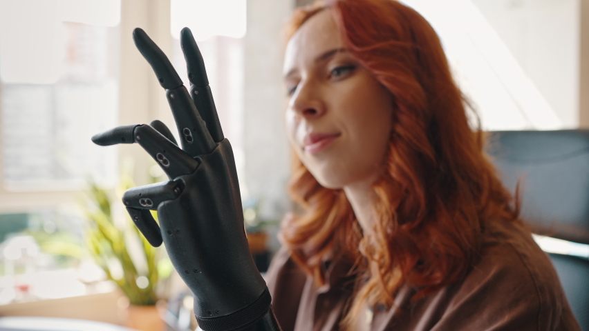 Portrait of a young attractive girl operating her robotic prosthesis, flexing and extending her fingers. Woman is controlling the bionic prosthesis. Bionics Cybernetic Robotic-arm Hand prosthesis. Royalty-Free Stock Footage #1074553559