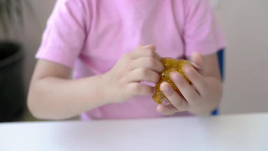 girl in a pink t-shirt stirring yellow slime golden granules sprinkling. child playing with a slime toy. DIY concept