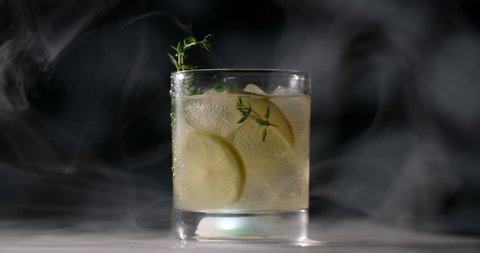 Cold glass with cocktail is spinning slowly in the smoke on the dark background, alcohol drinks and beverage, non-alcohol cocktail, object video of lemonade, 4k Prores HQ